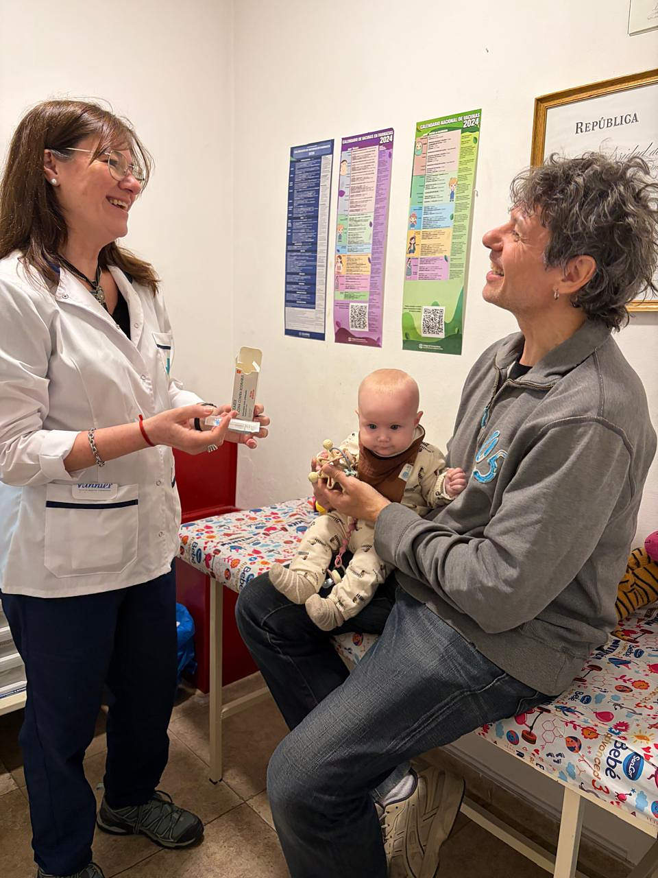 Farmacéutica de Farmacia Añon mostrándole una vacuna a un papá con su bebé en brazos en el vacunatorio
